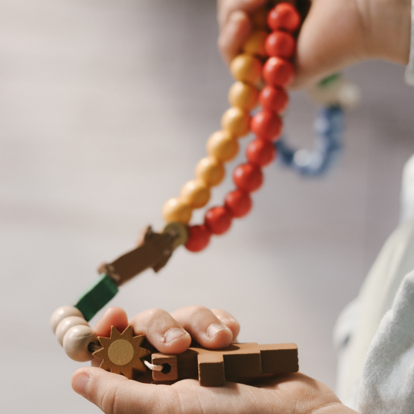 Close-up of hands holding a colorful wooden teething toy with beads and animal shapes.